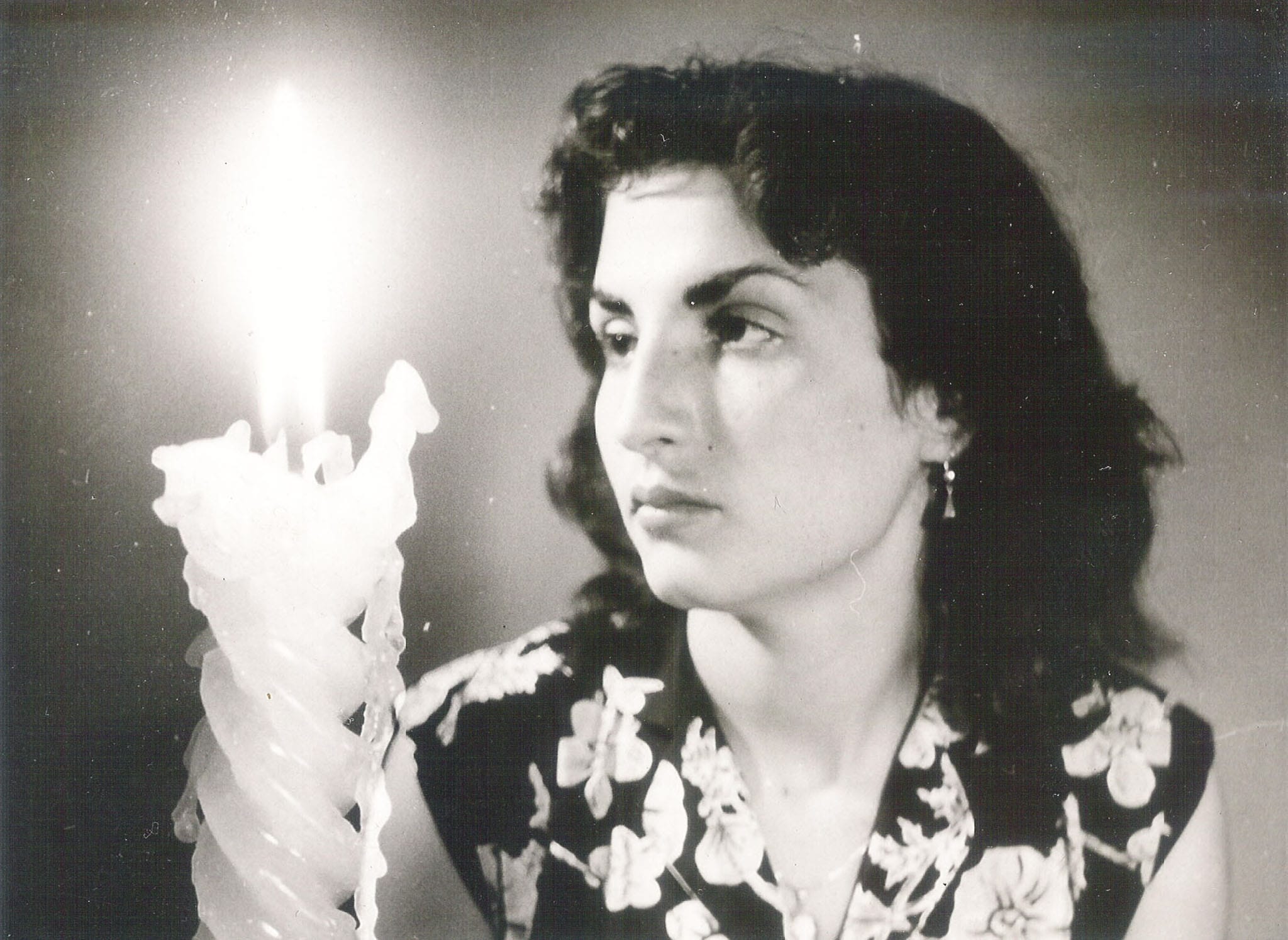 A black and white close-up portrait of a woman looking thoughtfully past a large, lit decorative candle.