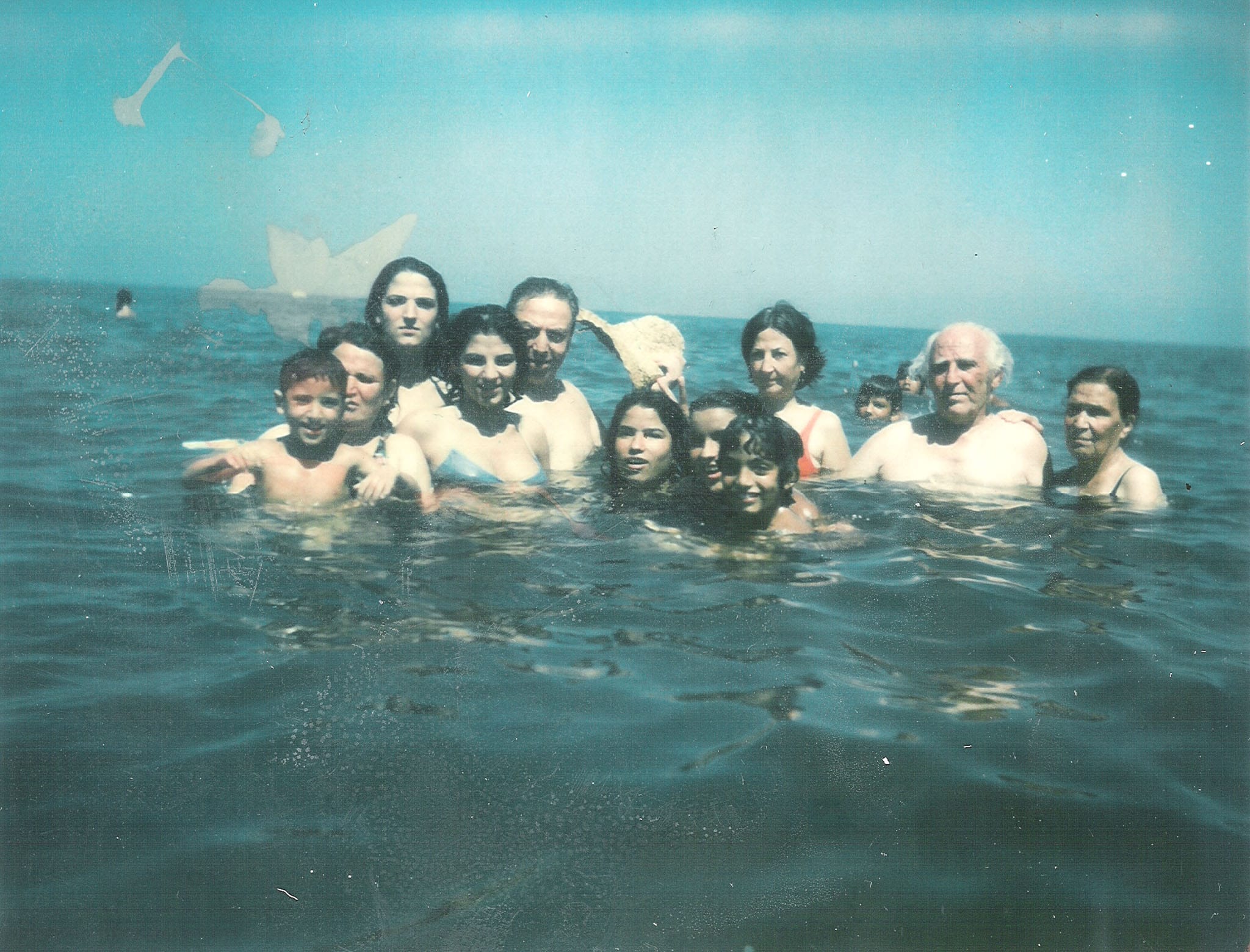 A large multi-generational family, including children and seniors, smiling while swimming together in the blue waters of the Caspian Sea.